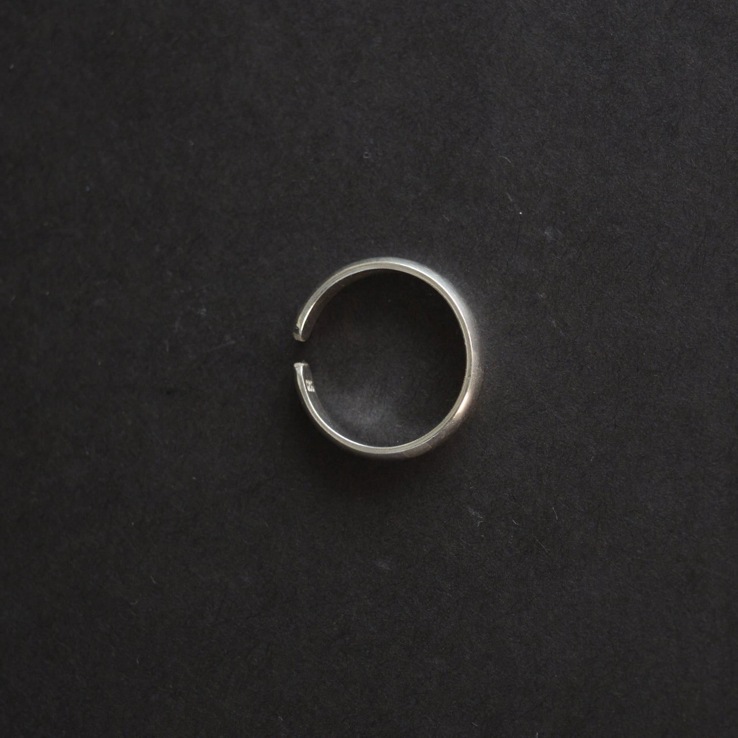 Top-down view of a polished silver band ring showing the adjustable gap and "925" hallmark stamp on a black background.