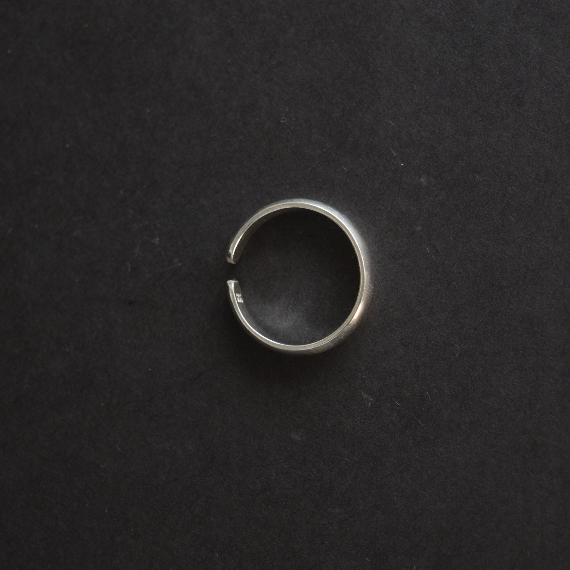 Top-down view of a polished silver band ring showing the adjustable gap and "925" hallmark stamp on a black background.