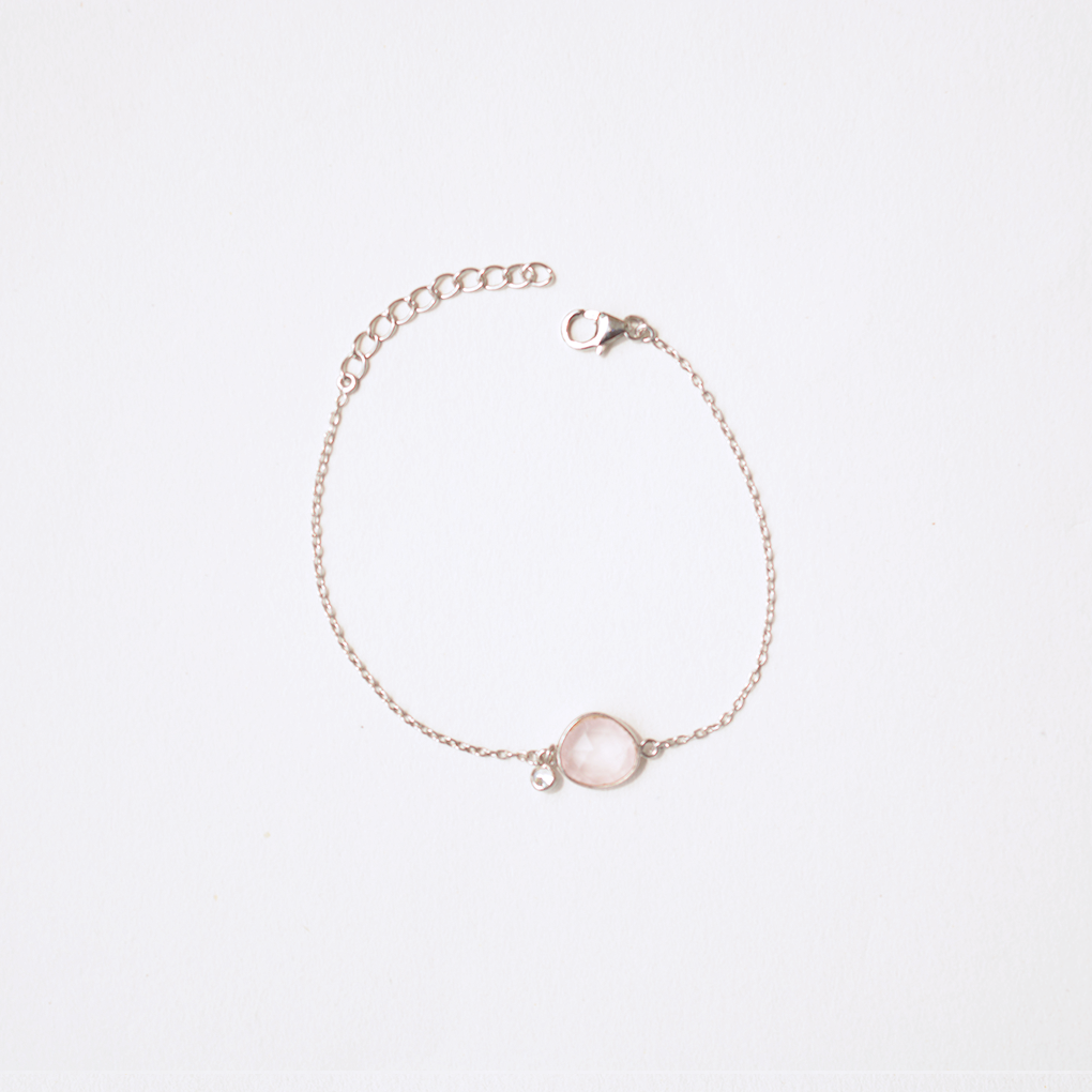 A fine silver chain bracelet with a dainty, smooth-cut rose quartz charm, set against a soft, clean white background.