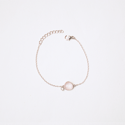 A fine silver chain bracelet with a dainty, smooth-cut rose quartz charm, set against a soft, clean white background.