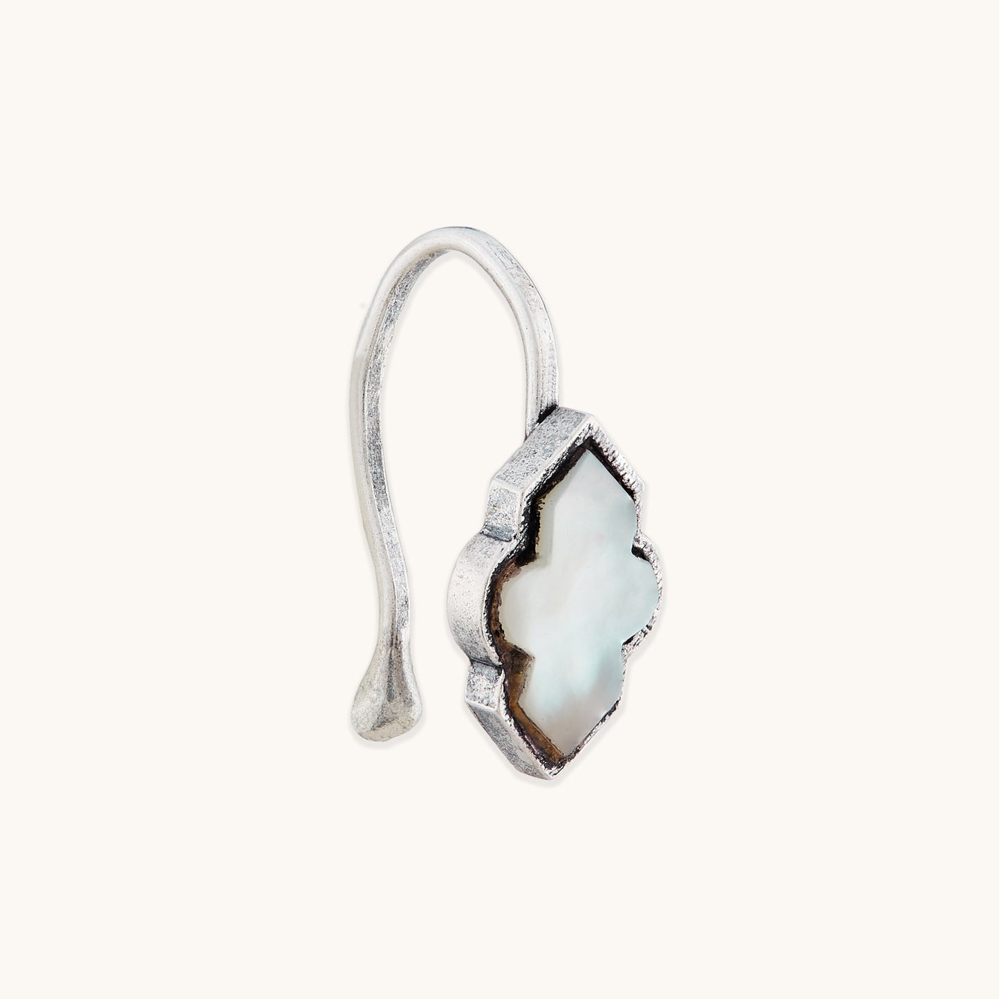 An angled view of an antique-finish silver clip-on nose accessory with an ornate, white, quatrefoil-shaped inlay.