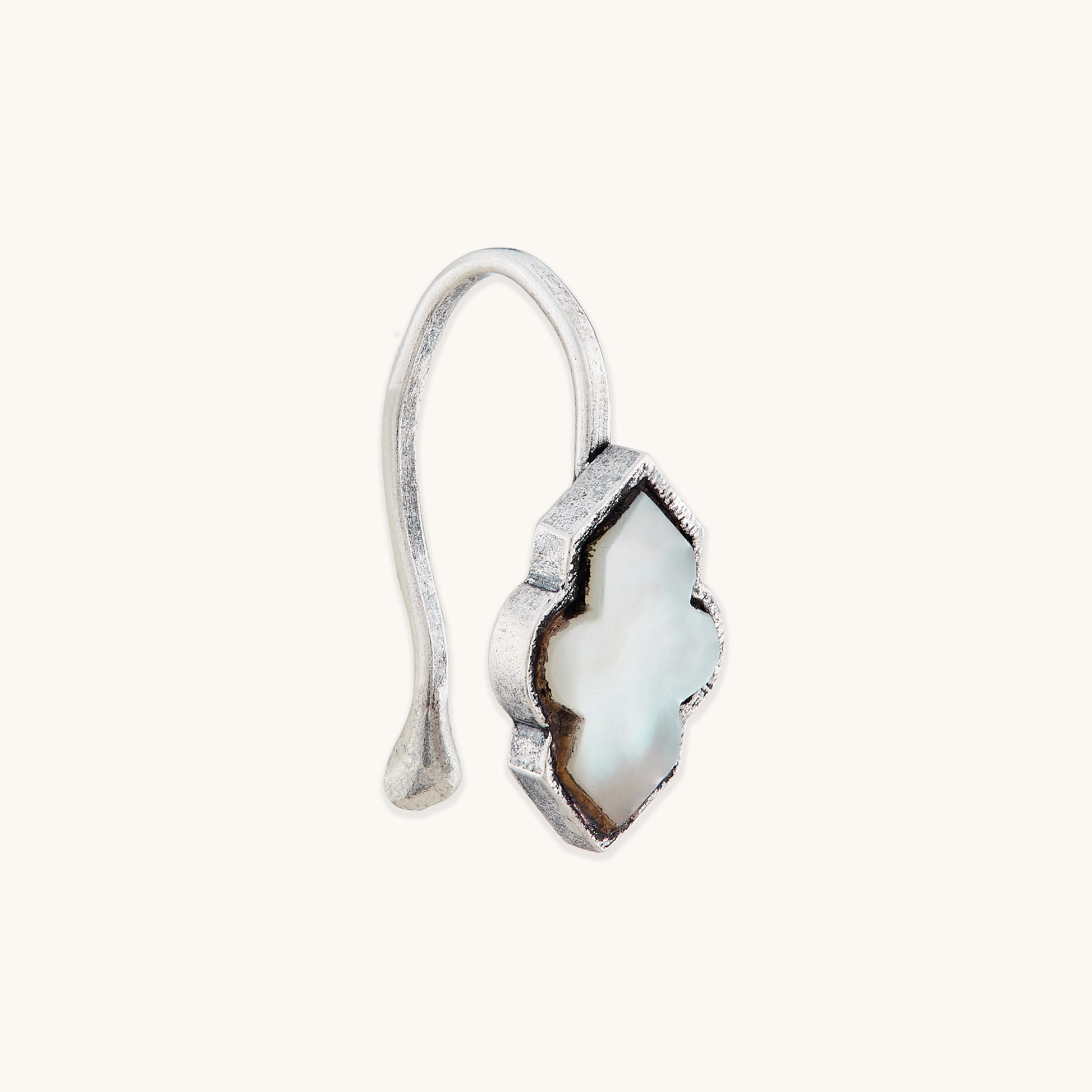 An angled view of an antique-finish silver clip-on nose accessory with an ornate, white, quatrefoil-shaped inlay.