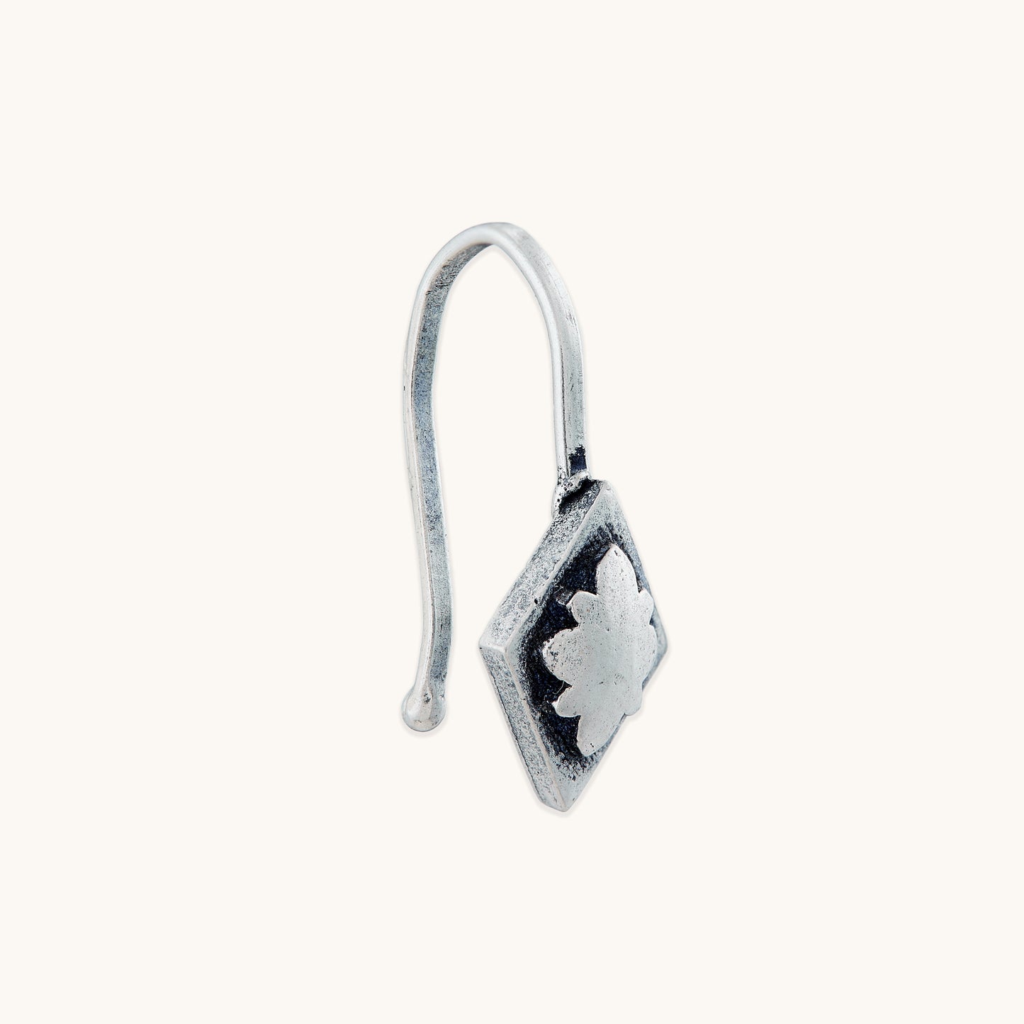 An angled side view of a diamond-shaped silver clip-on, highlighting the embossed floral texture and the structure of the attached silver hook.