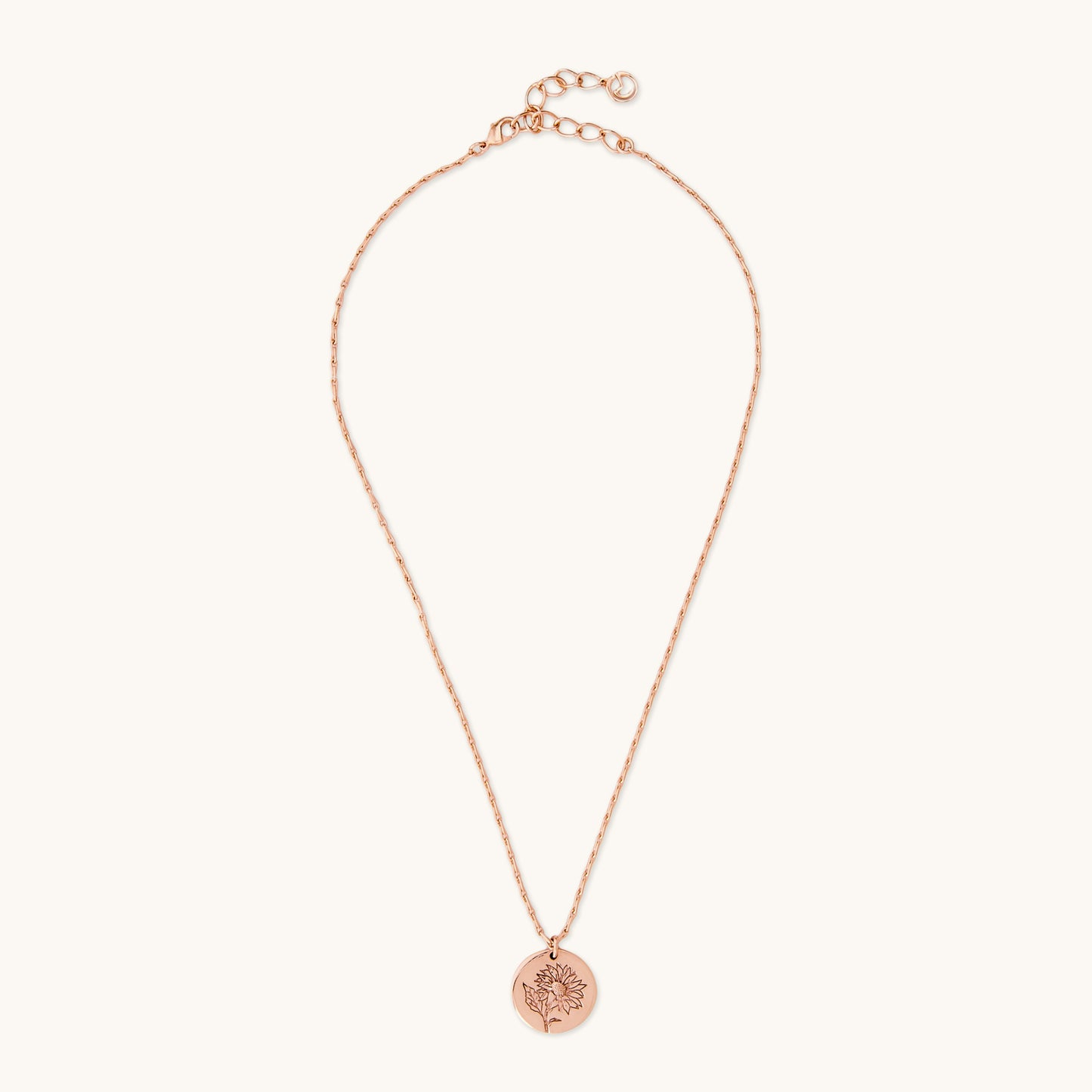 Full view of a delicate rose gold necklace with a circular sunflower medallion pendant, photographed on a white background.