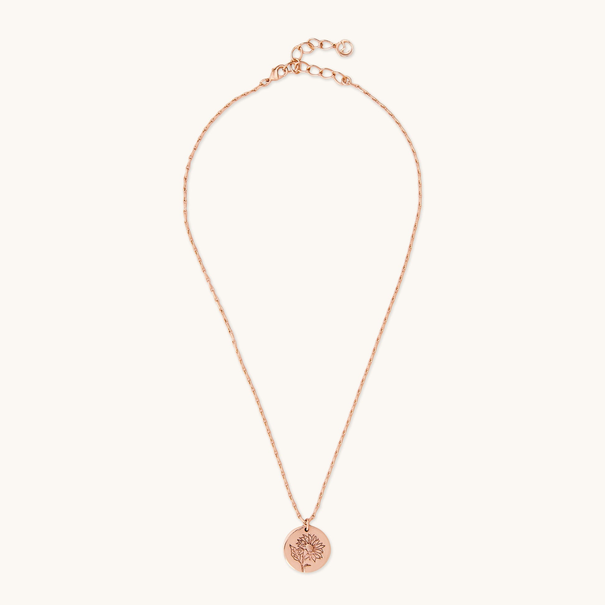 Full view of a delicate rose gold necklace with a circular sunflower medallion pendant, photographed on a white background.