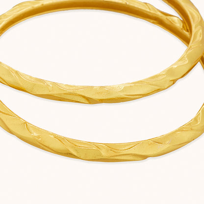 A macro close-up of Unstoppable Infinity Bangles showcasing an intricate, filigree vine pattern on a light surface.
