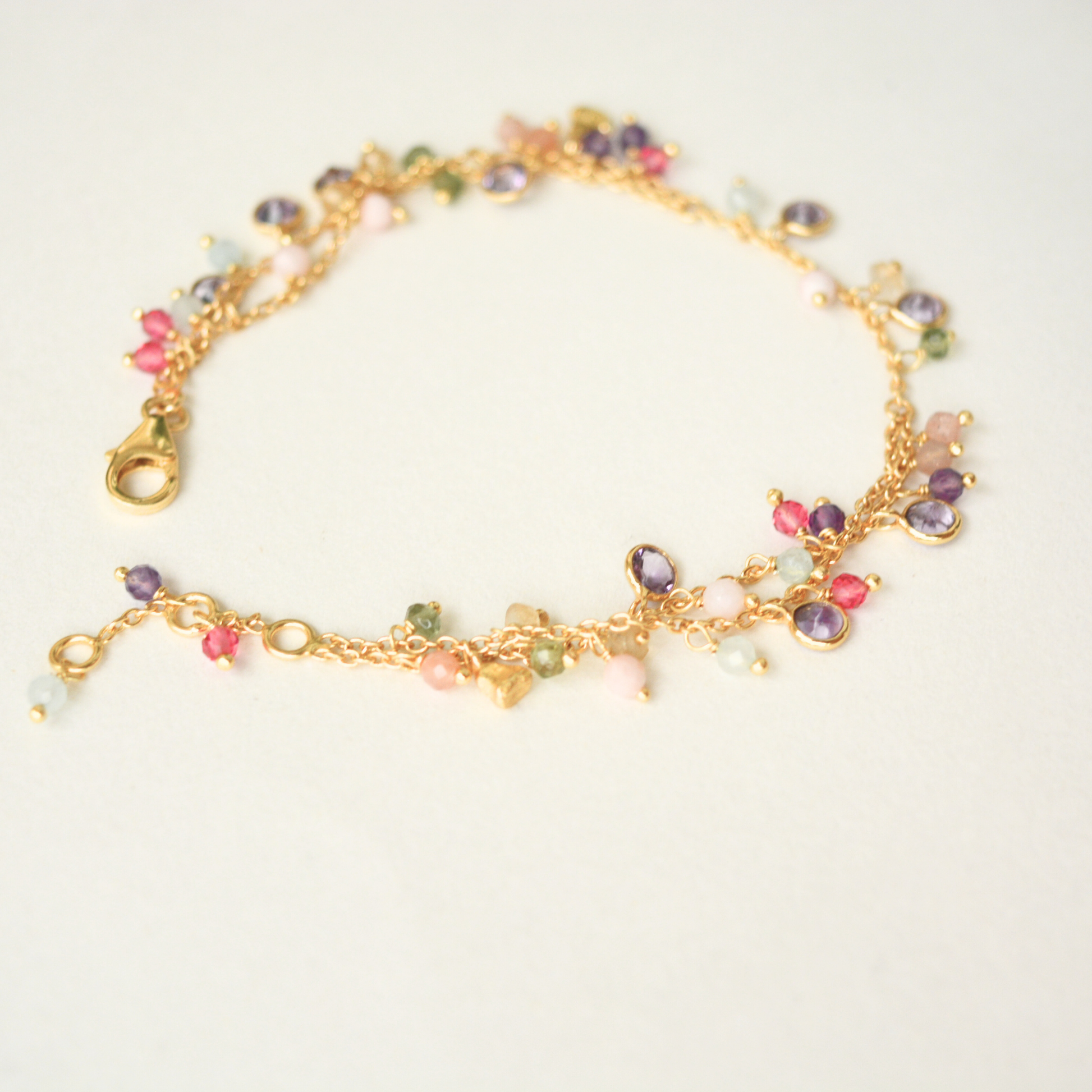A detail shot of the gold-plated double-chain bracelet, highlighting the various shapes and colors of the dangling gemstone charms.