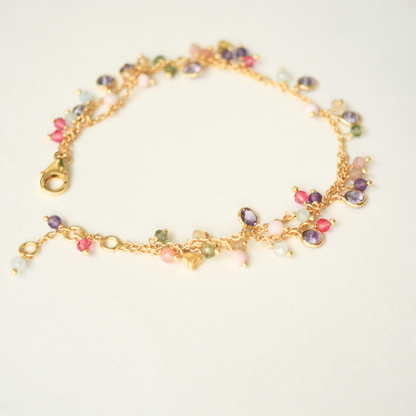 A detail shot of the gold-plated double-chain bracelet, highlighting the various shapes and colors of the dangling gemstone charms.