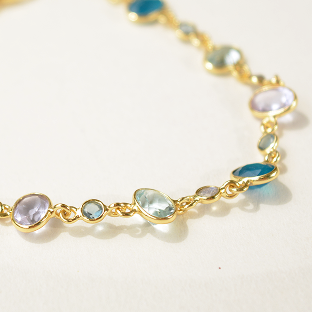 Close-up of a minimalist silver bracelet with vibrant blue and green gemstone accents, isolated on a white background.