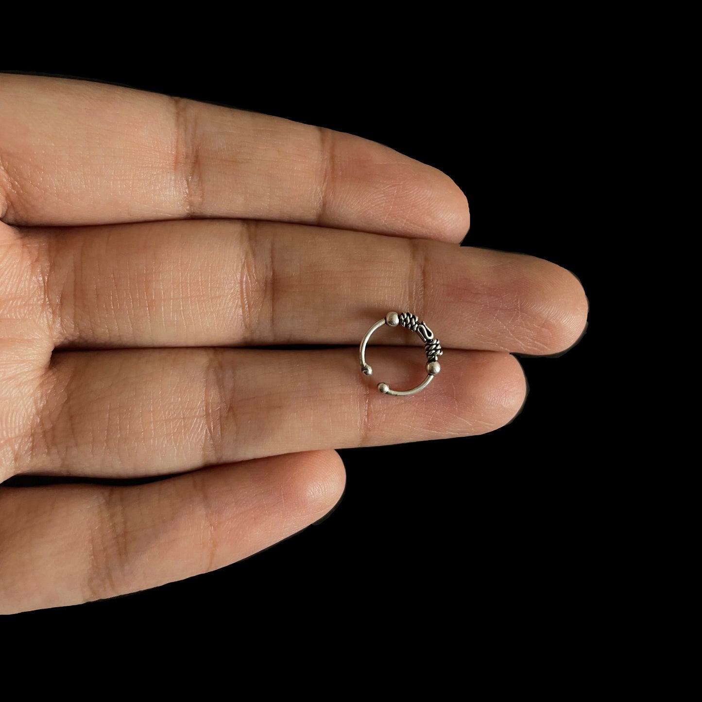 A hand holding a circular, 925 sterling silver bohemian-style hoop with detailed braided and beaded metalwork.
