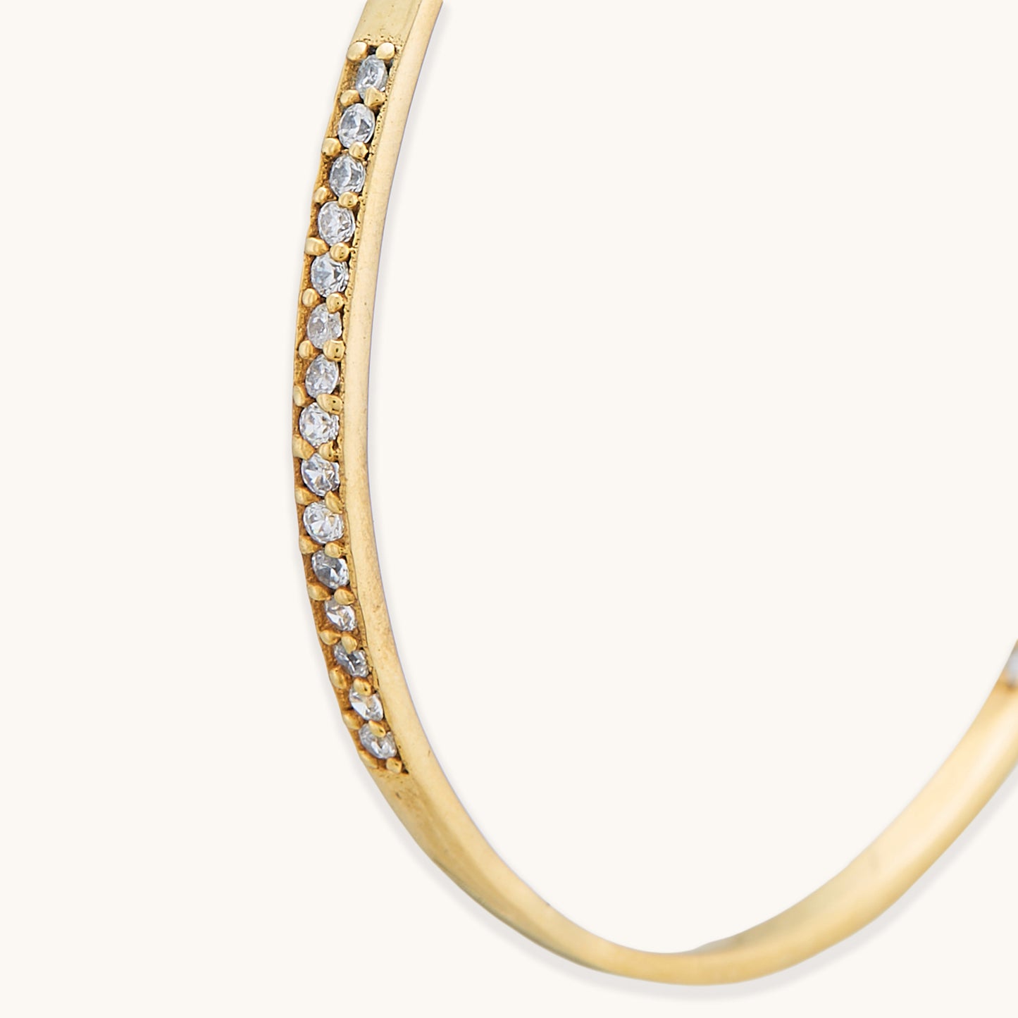 A close-up studio shot of a gold-plated hoop earring with a thick, asymmetrical silhouette and a polished high-shine finish.