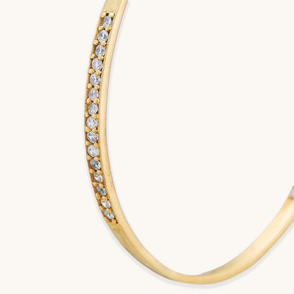 A close-up studio shot of a gold-plated hoop earring with a thick, asymmetrical silhouette and a polished high-shine finish.