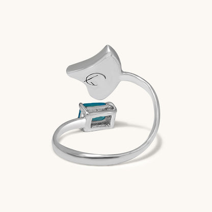A back-view studio photograph of an open silver ring, showing the structural band and the underside of the triangular abalone shell inlay and the blue gemstone setting.