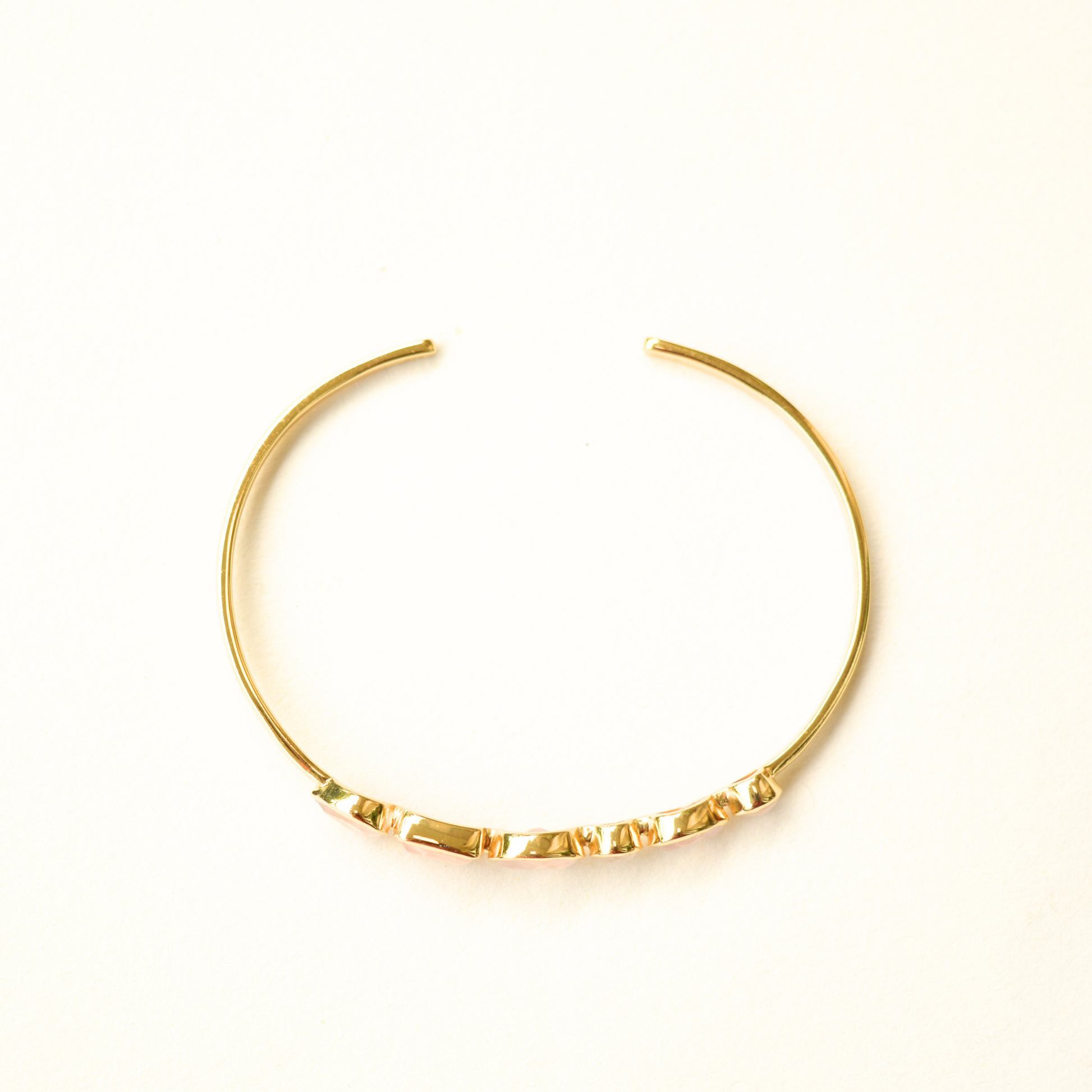A top view of a gold-plated cuff bracelet showcasing its open-style silver metal band.