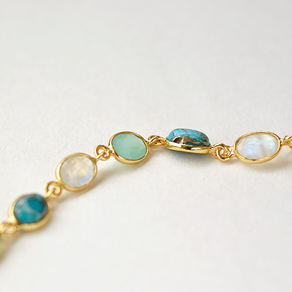 Close-up of a delicate silver bracelet with a row of polished blue-toned gemstone charms, isolated on a white background.