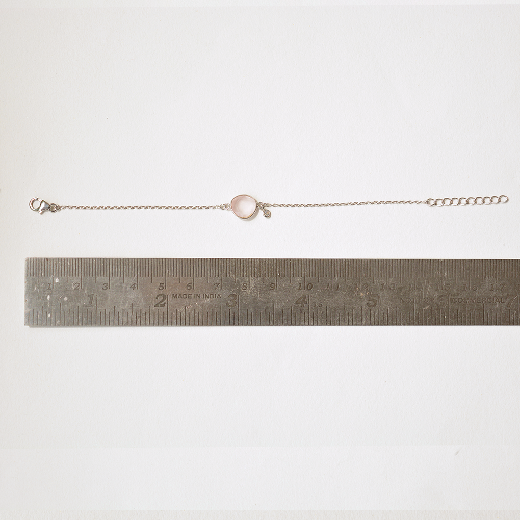 Top-down view of a delicate silver jewelry piece with a heart-soft pink gemstone, highlighting the adjustable slider mechanism for a perfect fit.