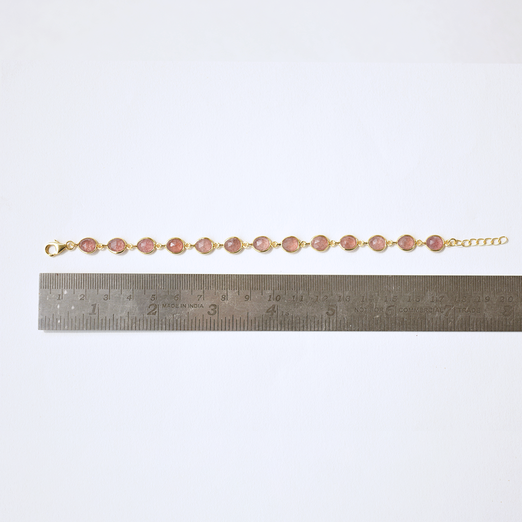 A minimalist silver bracelet with a speckled reddish-pink stone, isolated on a white background.