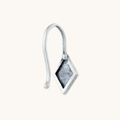 A close-up studio shot of the back of a diamond-shaped silver clip-on, showing the recessed metal texture and the attached silver hook.