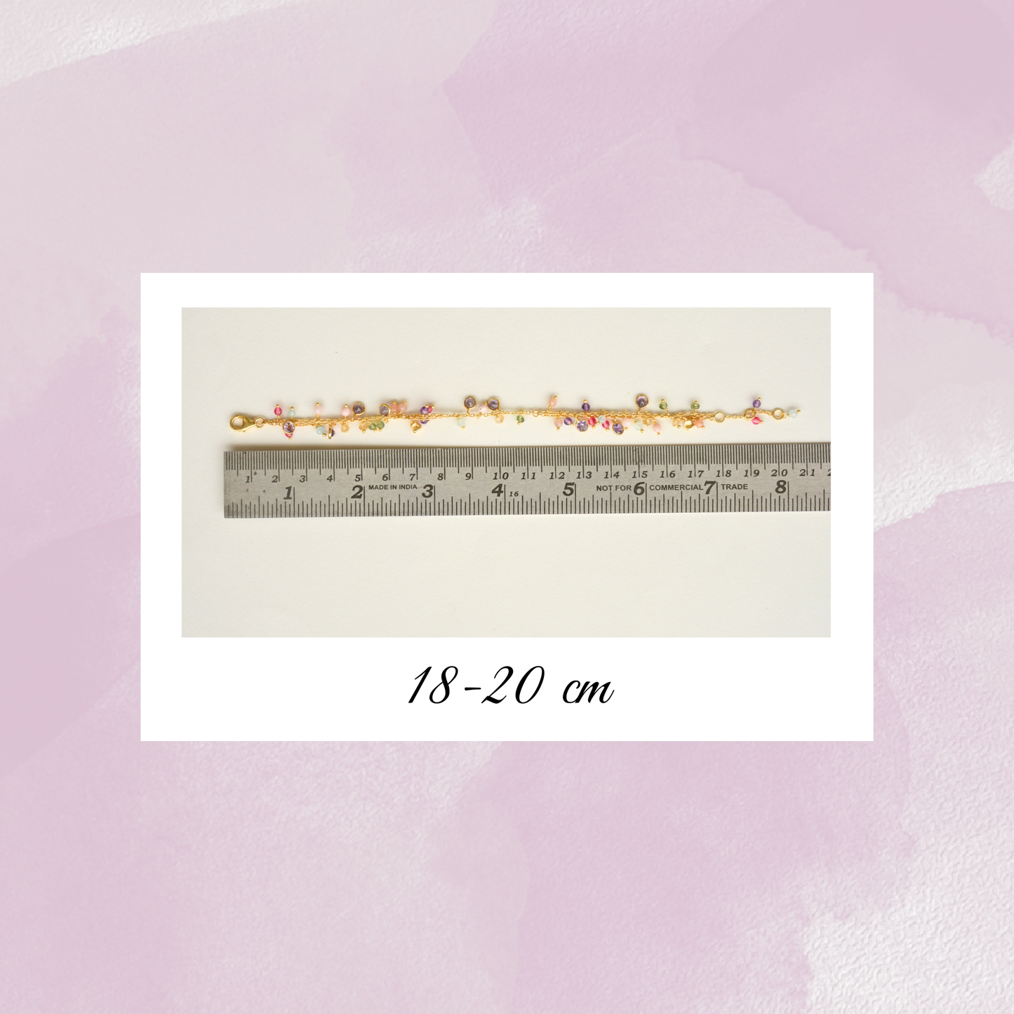 A gold-plated silver charm bracelet displayed against a metal ruler, indicating an adjustable length between 18 and 20 cm.