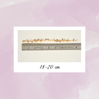 A gold-plated silver charm bracelet displayed against a metal ruler, indicating an adjustable length between 18 and 20 cm.