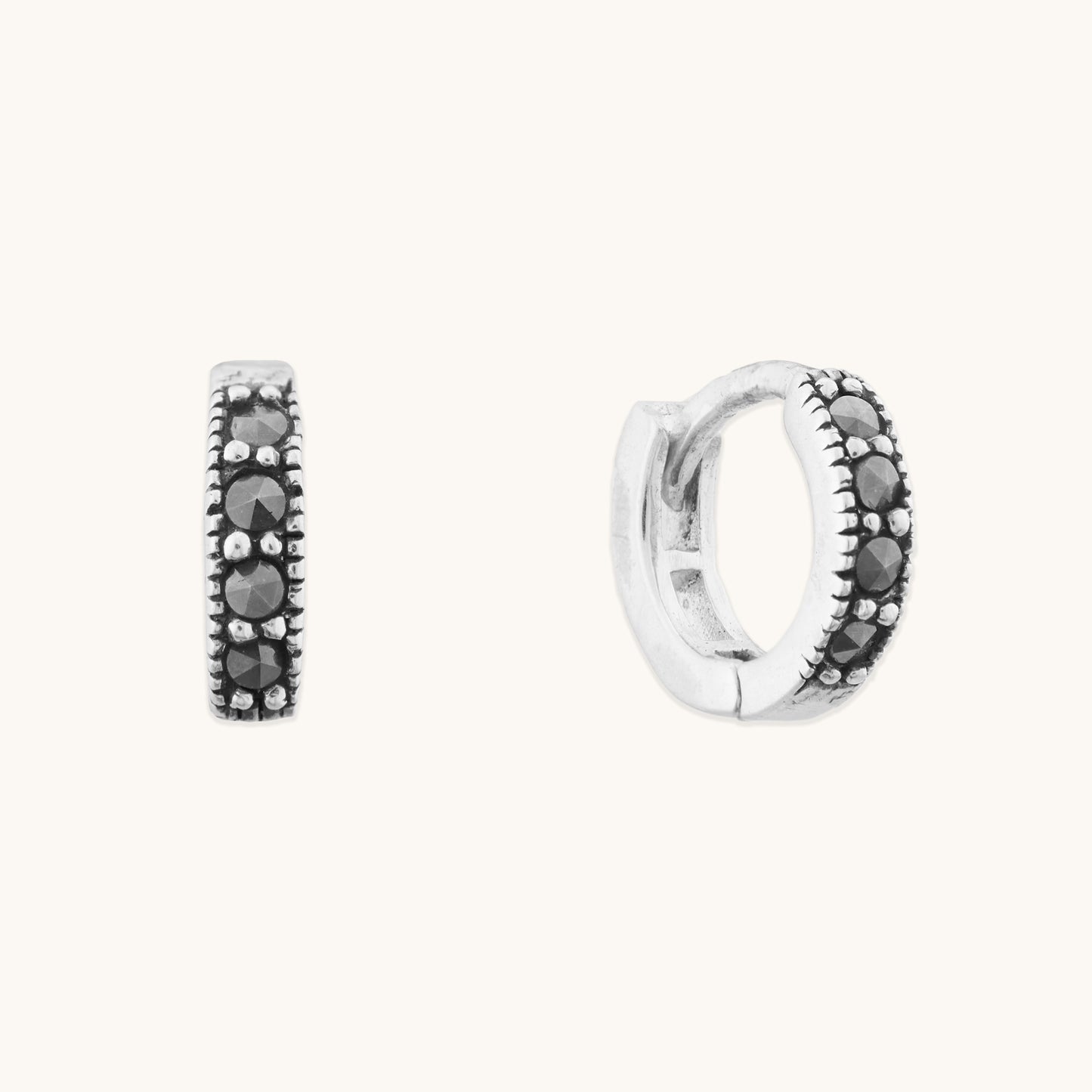 Minimalist silver jewelry featuring dainty hinged hoops with sparkling black accents for a stacked ear look.