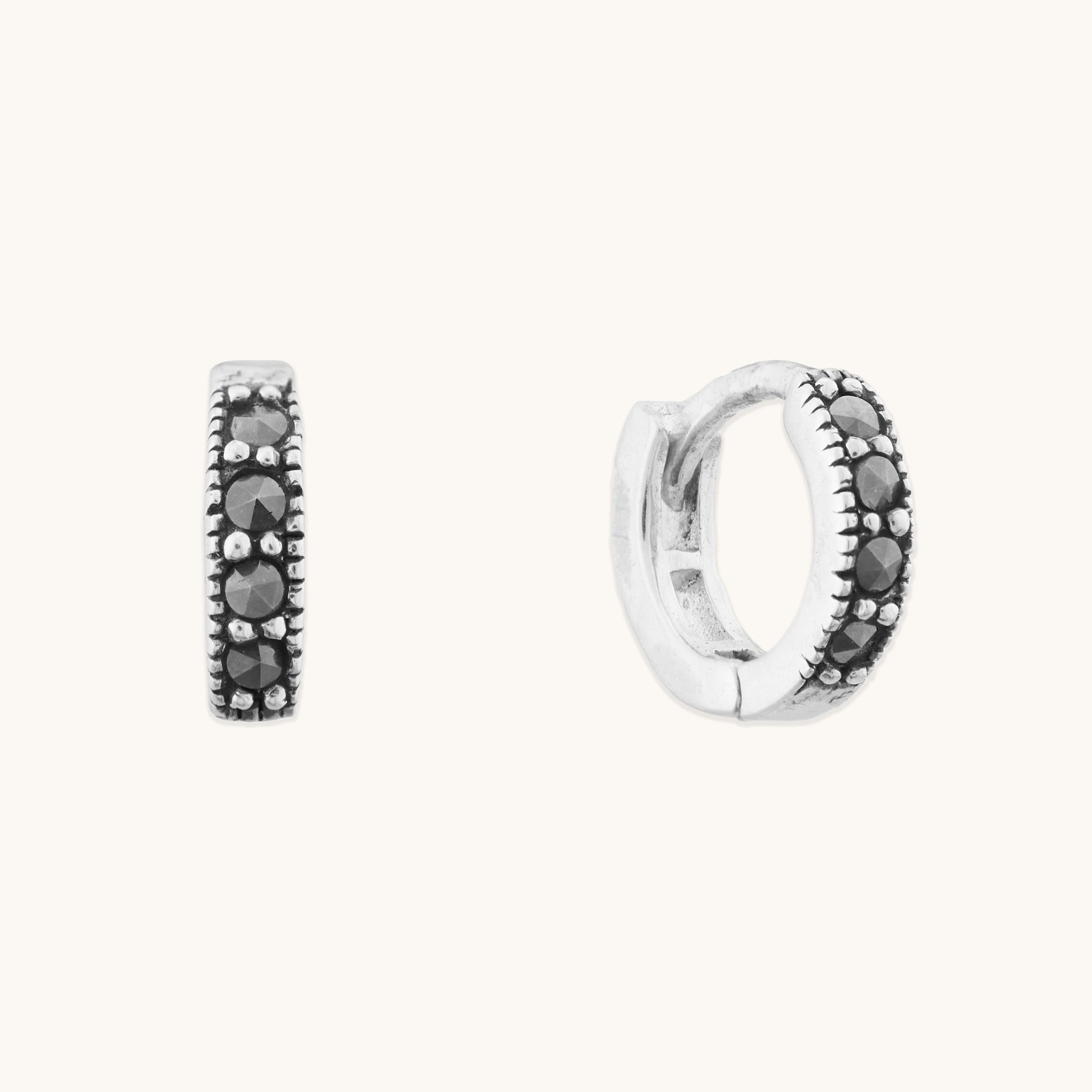 Minimalist silver jewelry featuring dainty hinged hoops with sparkling black accents for a stacked ear look.