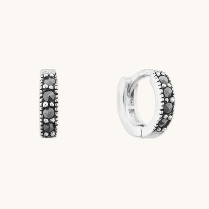 Minimalist silver jewelry featuring dainty hinged hoops with sparkling black accents for a stacked ear look.