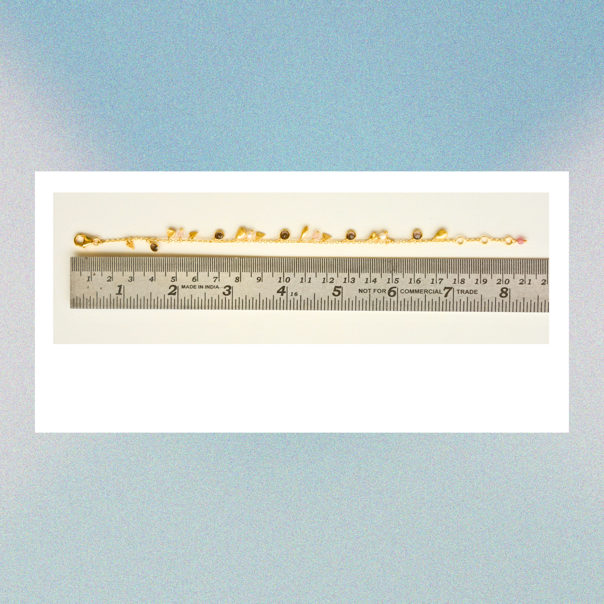 The charm-adorned gold-plated silver bracelet displayed next to a metal ruler to show an adjustable length of approximately 18 to 20 cm.