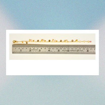 The charm-adorned gold-plated silver bracelet displayed next to a metal ruler to show an adjustable length of approximately 18 to 20 cm.