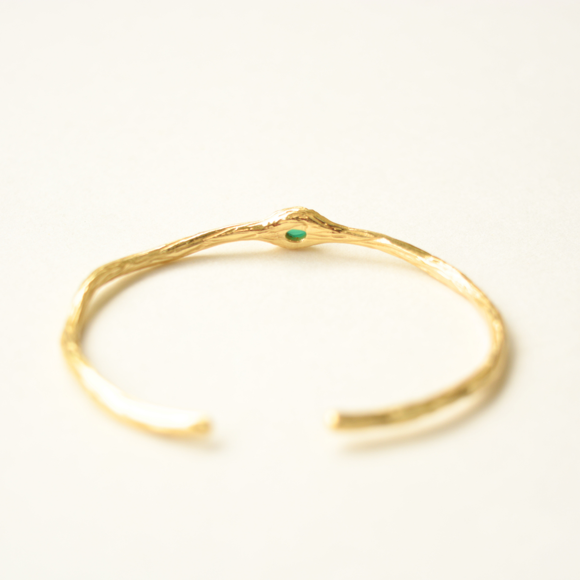 A close-up focus on the center green gemstone setting of a rustic, textured gold-toned bracelet.