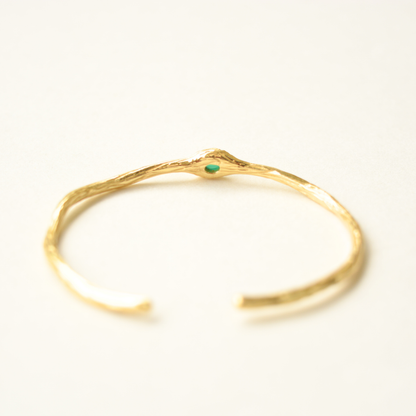 A close-up focus on the center green gemstone setting of a rustic, textured gold-toned bracelet.