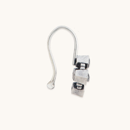 A direct side profile view of a silver-toned, geometric clip-on nose ring, focusing on the textured metallic edges.