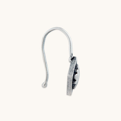A side-profile view of a diamond-shaped silver clip-on, focusing on the profile and depth of the embossed floral design and the curved hook shape.