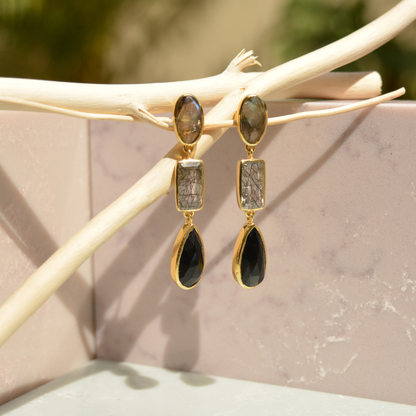 Close-up flat lay of the Midnight Elegance earrings on a white background, showcasing the iridescent labradorite tops and geometric black stone textures.