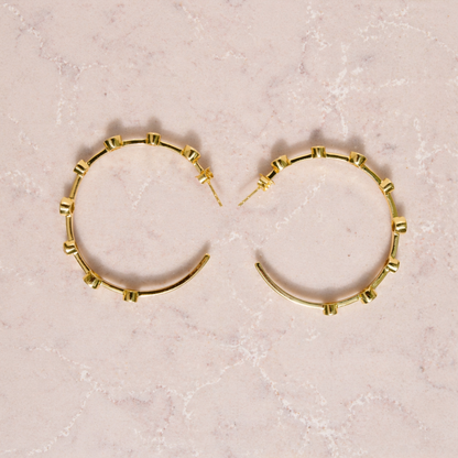 Top-down flat lay of the Moonspell Layers earrings in 18kt gold-plated 925 sterling silver on a textured stone surface.