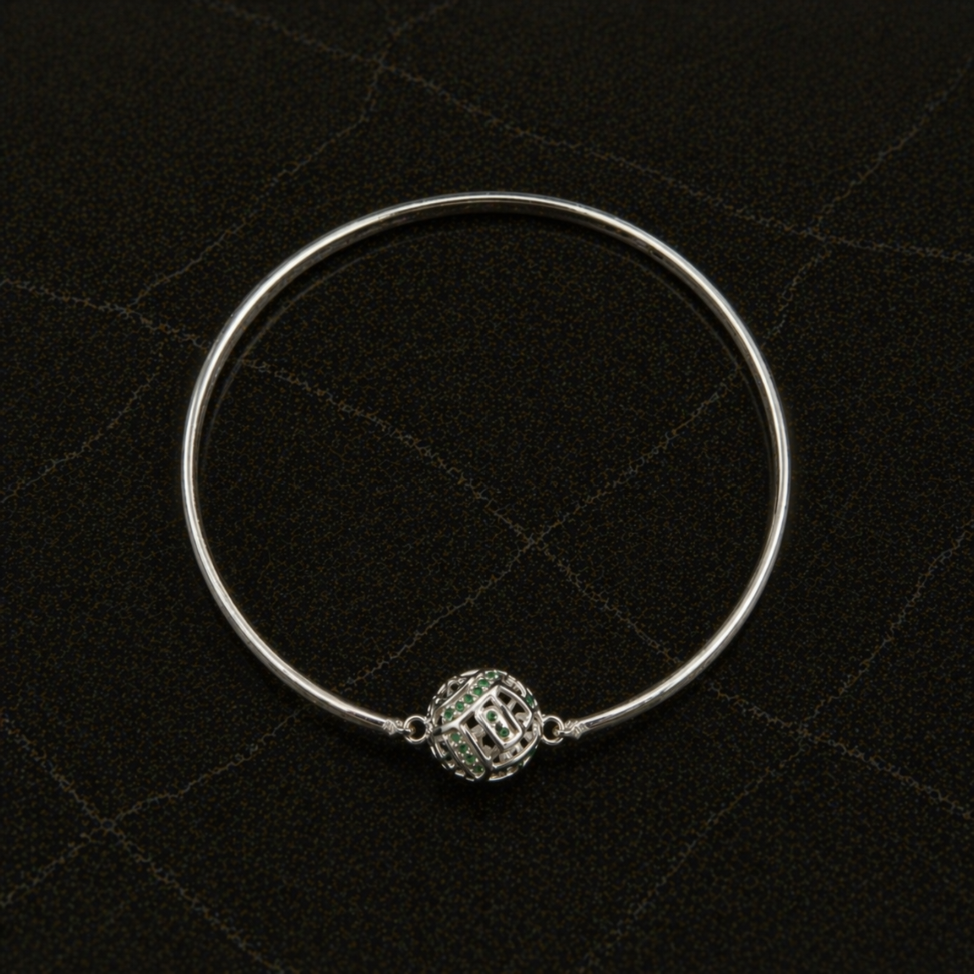 Top-down flat lay of the handcrafted Green Glow Rolling Bangle in rhodium-plated brass featuring a centered sphere with green CZ stones.