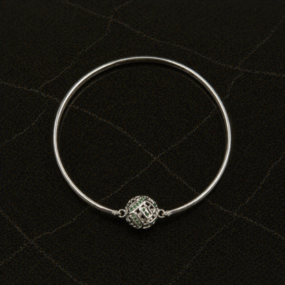 Top-down flat lay of the handcrafted Green Glow Rolling Bangle in rhodium-plated brass featuring a centered sphere with green CZ stones.