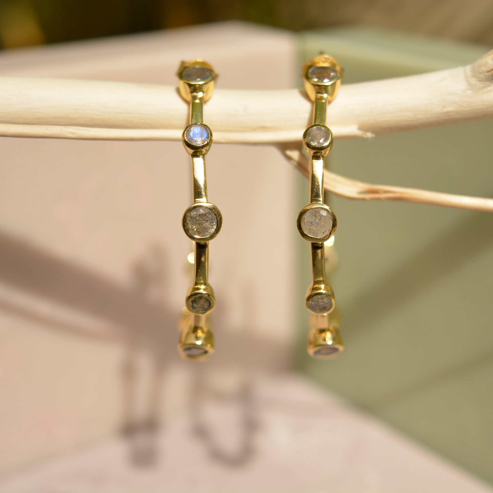 Close-up of the Moonspell Layers earrings hanging on a branch, highlighting the iridescent flashes of the natural labradorite stones.