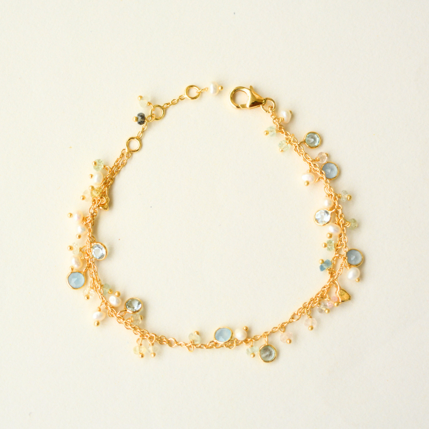 A delicate gold-plated silver double-chain bracelet accented with colorful gemstone and pearl charms, displayed on a clean white background.