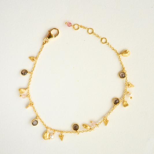 A delicate gold-plated silver chain bracelet featuring assorted irregular pebble-shaped charms, pearls, and clear quartz stones against a white background.