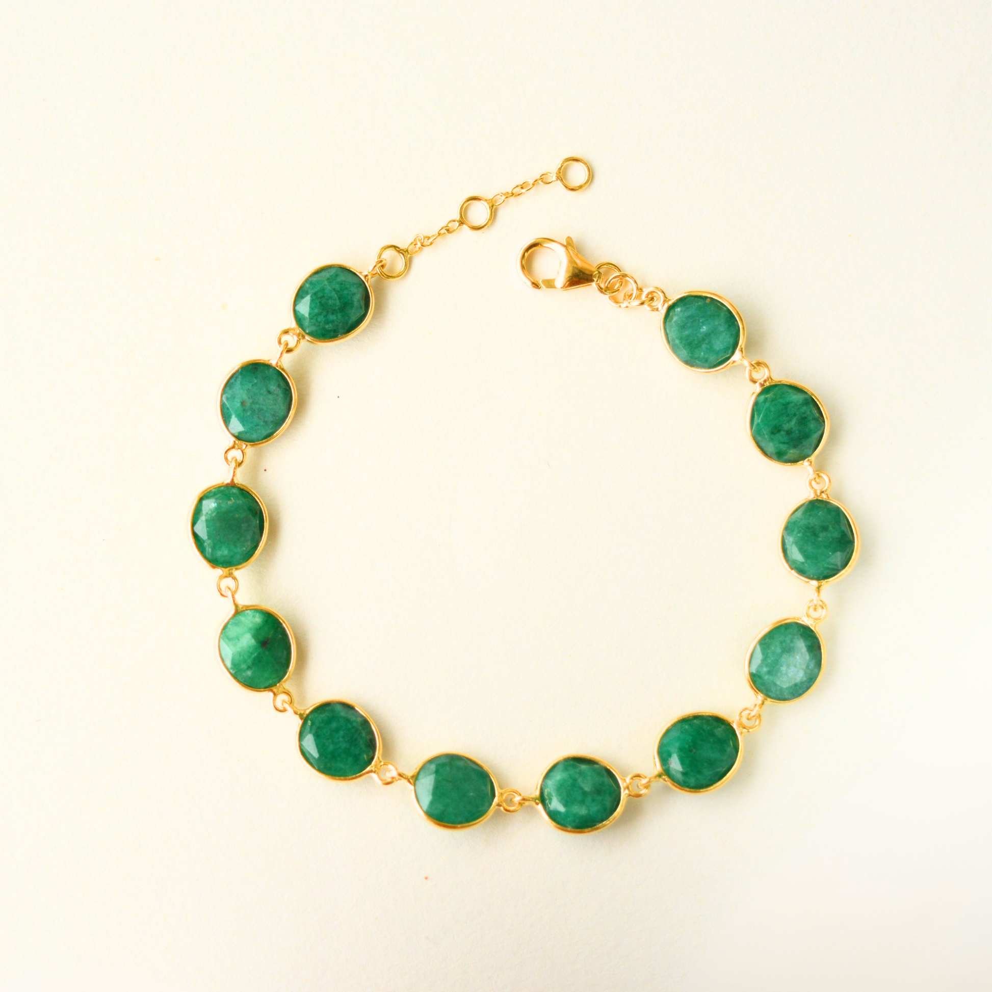 A top view highlighting the bezel-set, oval-cut green emerald stones connected by fine gold-plated silver links.