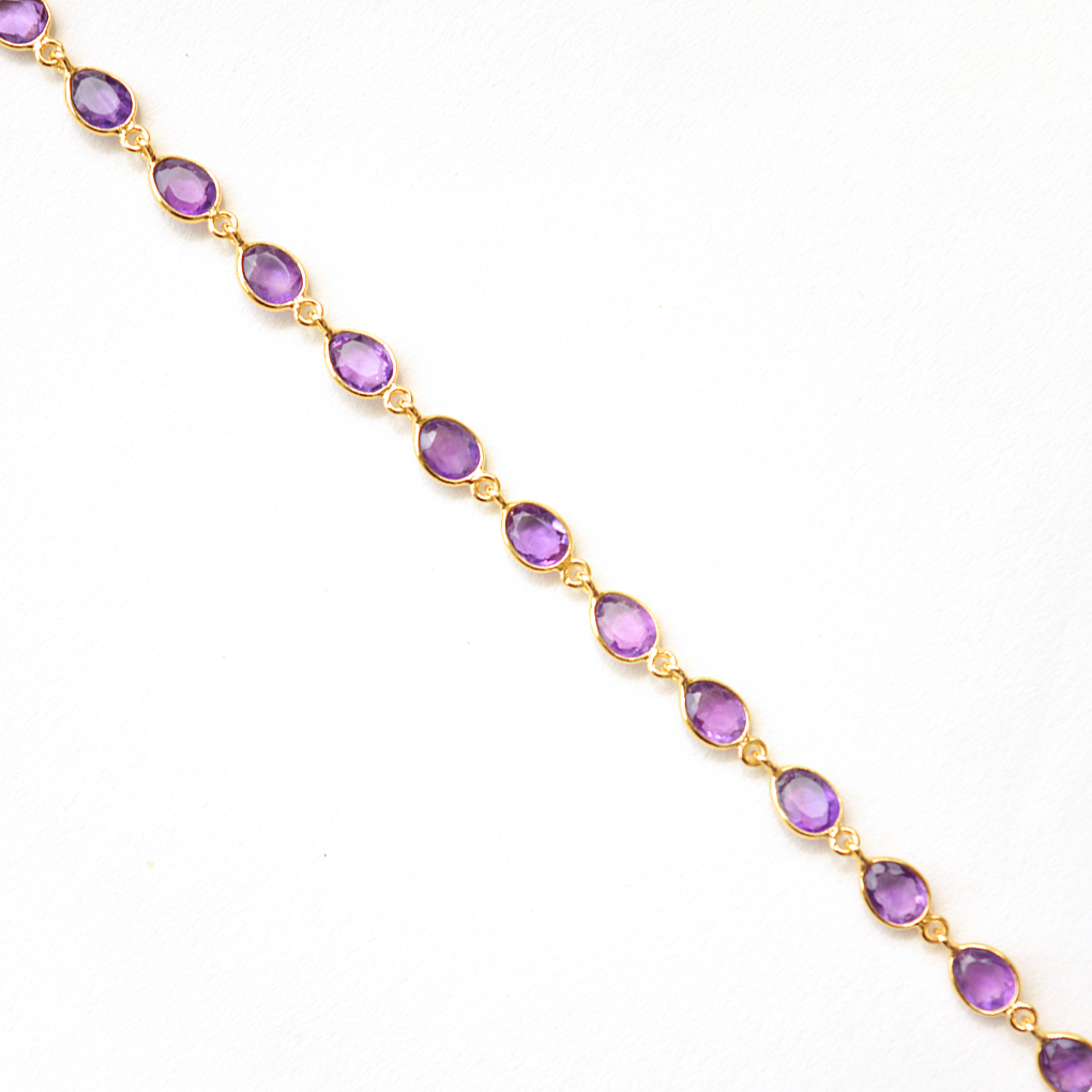 Close-up of a minimalist silver bracelet with a vibrant violet gemstone, isolated on white.