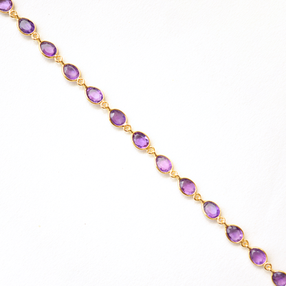 Close-up of a minimalist silver bracelet with a vibrant violet gemstone, isolated on white.