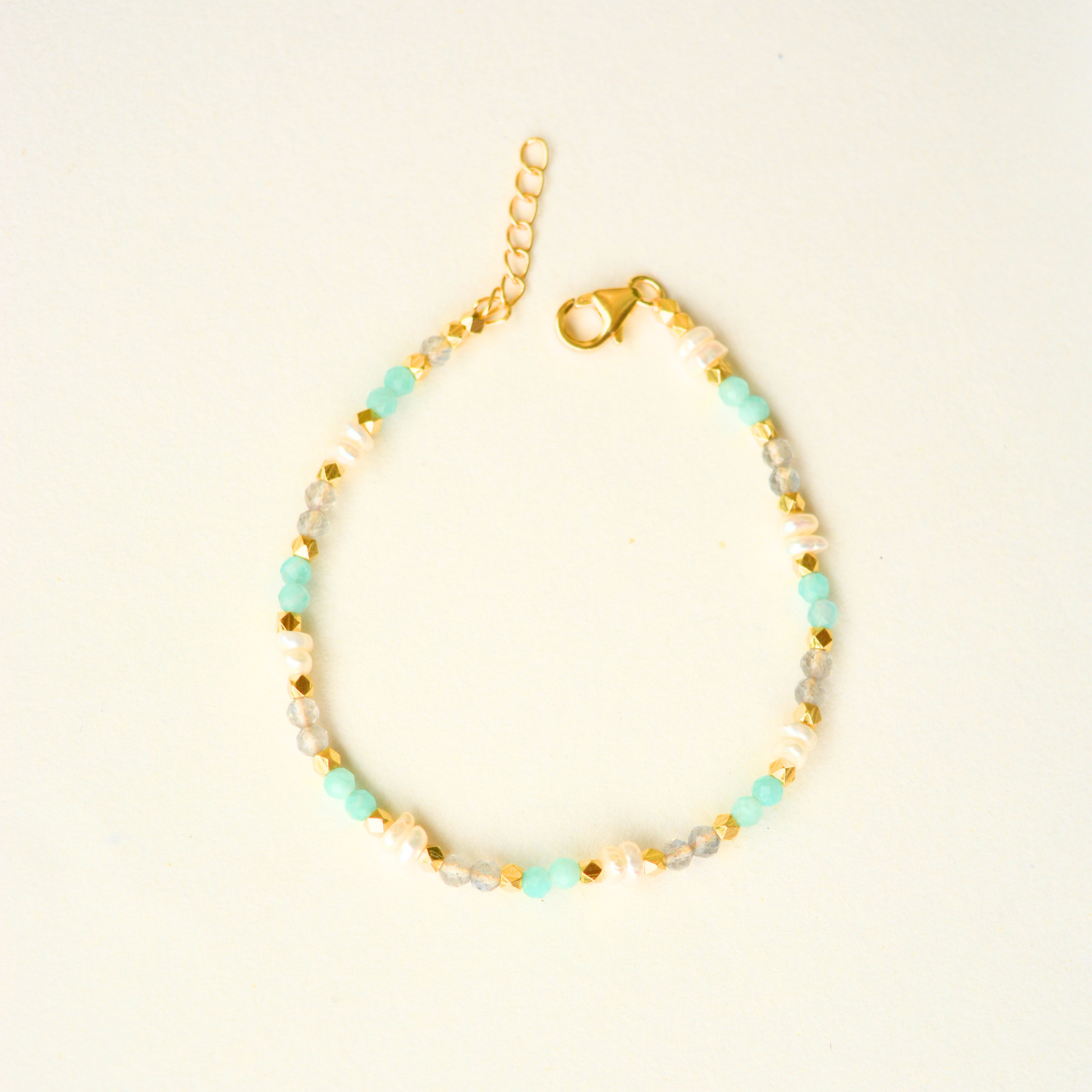 A gold-plated silver beaded bracelet featuring alternating light blue stones, pearls, and small metallic gold spacers, set against a plain background.