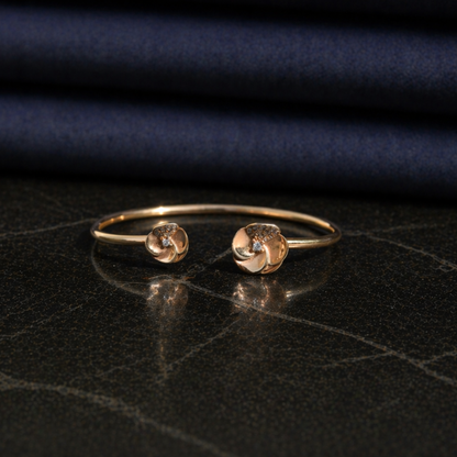 Front view of the adjustable Blushing Blooms Bangle, showcasing the polished rose gold finish and two CZ-studded flower ends on a dark marble surface.