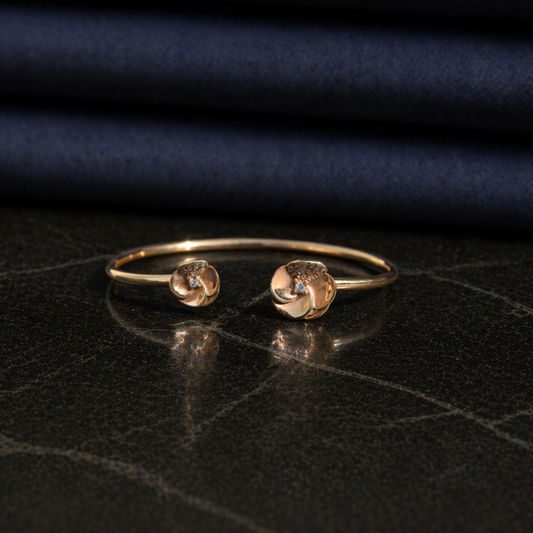 Front view of the adjustable Blushing Blooms Bangle, showcasing the polished rose gold finish and two CZ-studded flower ends on a dark marble surface.