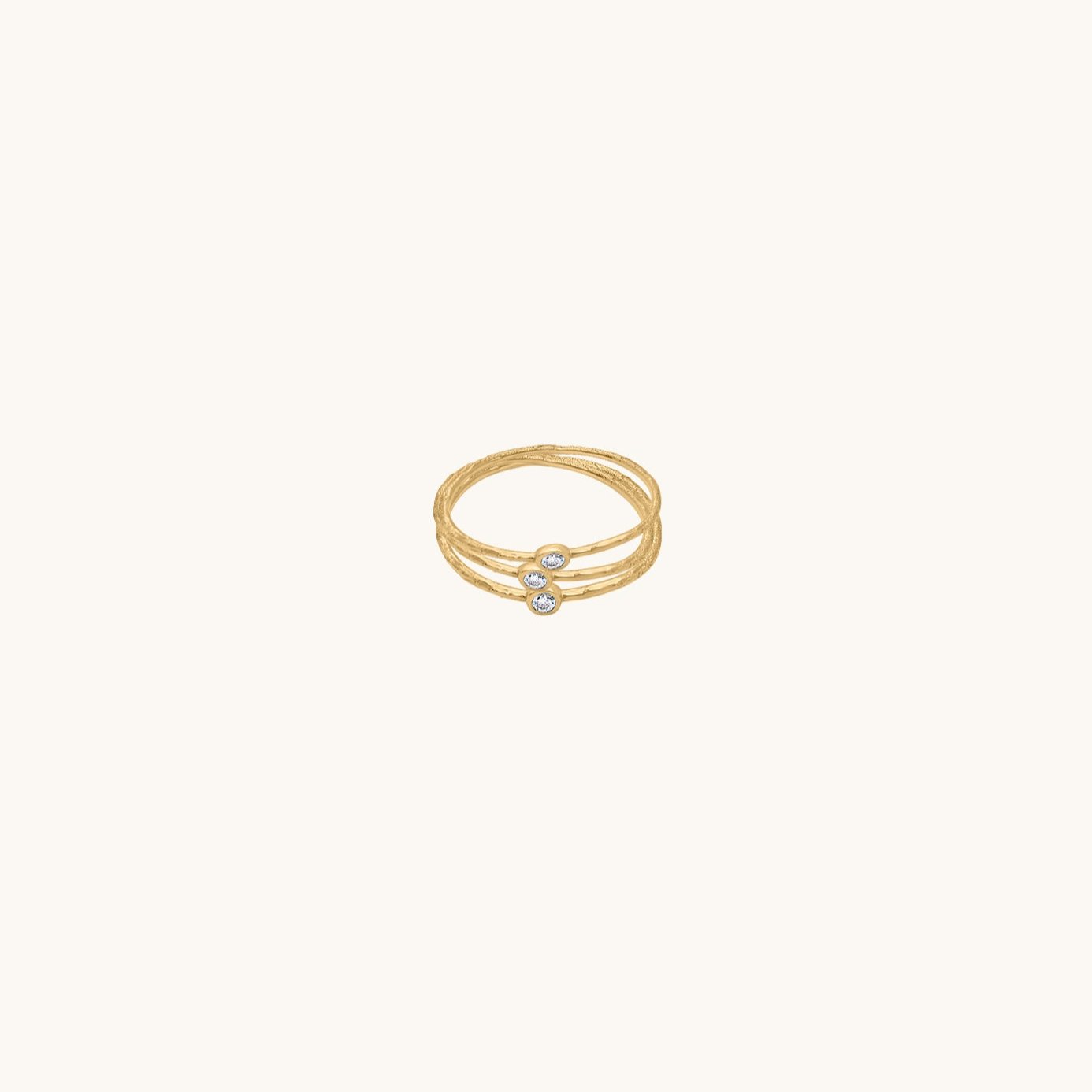 A trio of textured gold stacking rings with sparkling round-cut stones, featuring an organic hammered finish on a neutral background.
