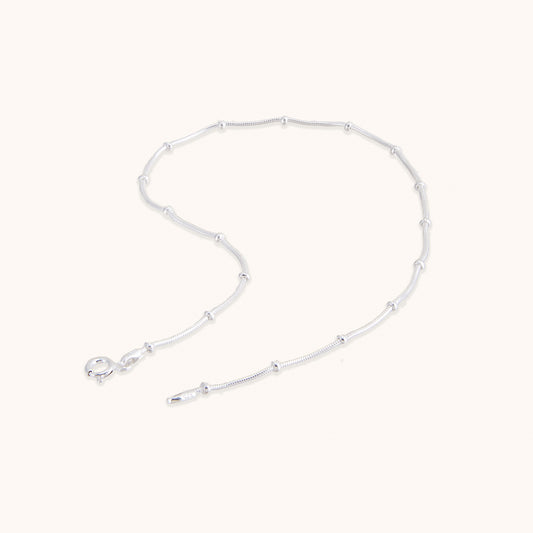 A delicate, minimalist silver chain featuring evenly spaced small beads along the strand, shown with a secure clasp.