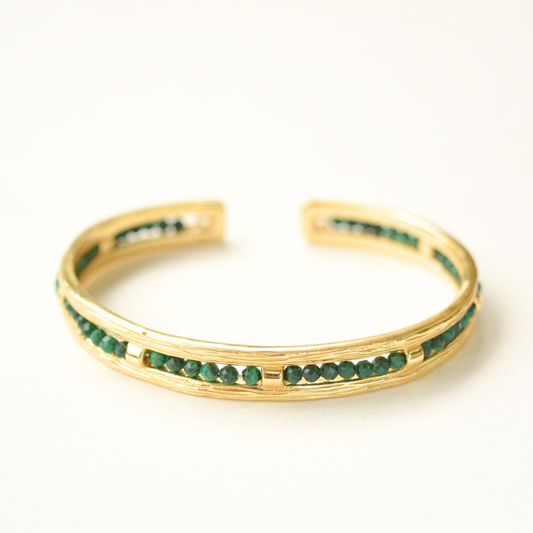 Gold-plated open cuff bracelet featuring a detailed textured metal band and a row of embedded emerald beads.