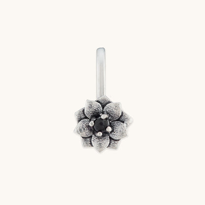 A front-facing studio shot of a silver-toned, floral-shaped nose clip featuring an intricate petal design and a dark, polished center stone.